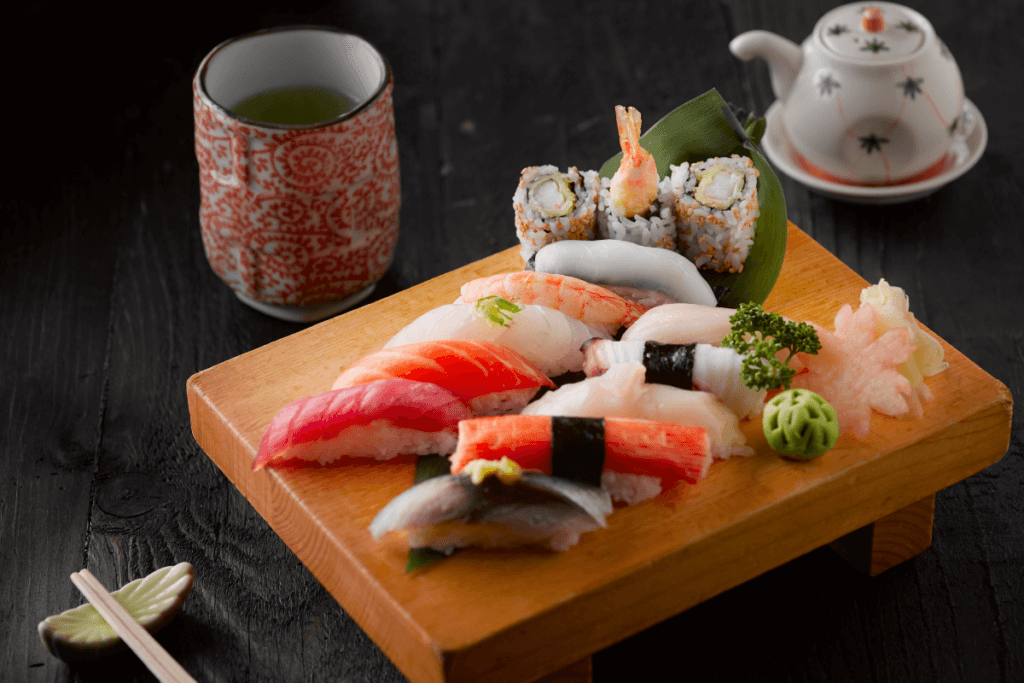 12 assorted nigiri sushi pieces on a wooden platter with a cup of green tea and chopsticks, traditional Japanese cuisine"